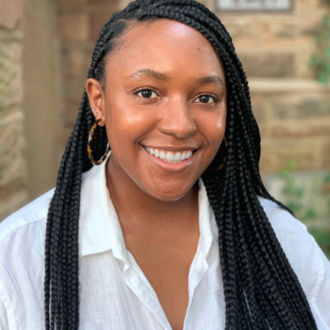 woman with braids in white linen shirt in front of a stone wall