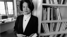 Black and white image of Saville in front of a bookshelf in a white turtleneck