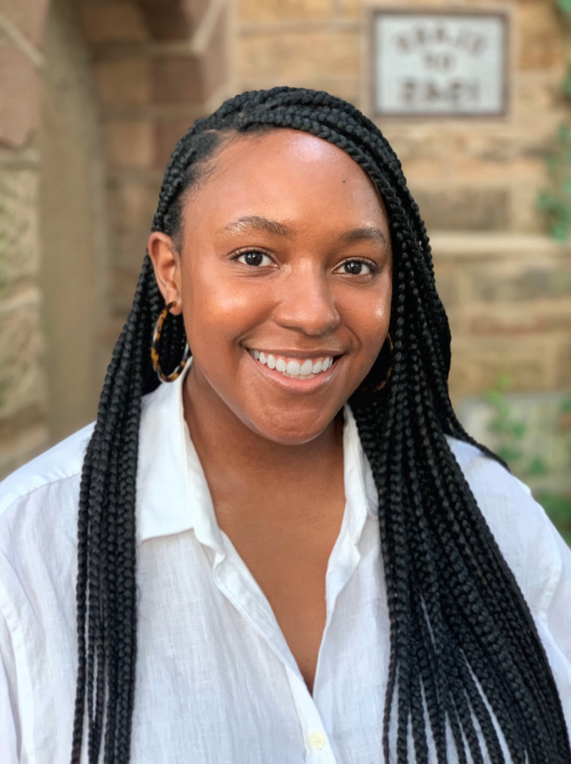 woman with braids in white linen shirt in front of a stone wall