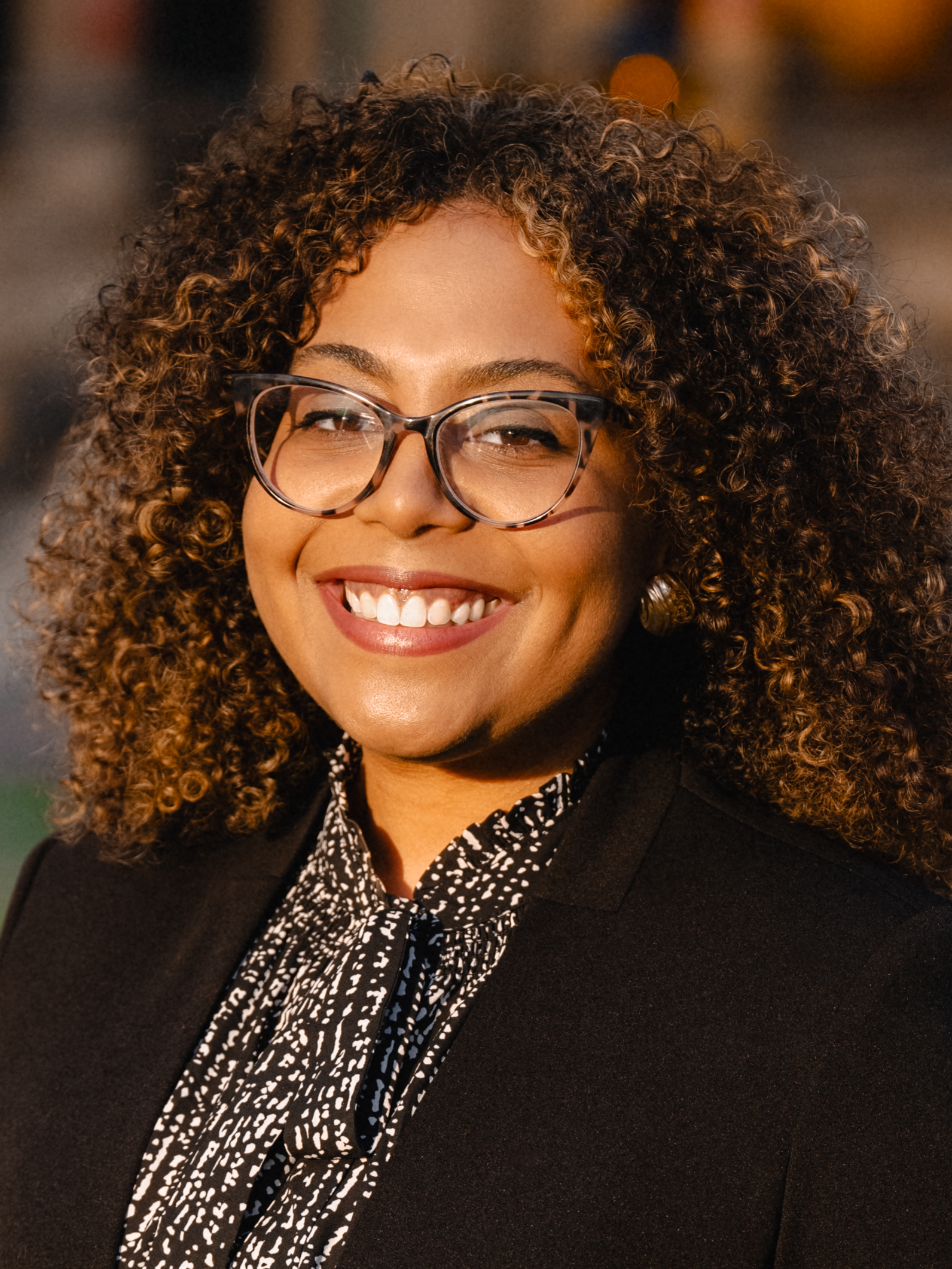 headshot of a woman in a printed shirt and black blazer with tortoise shell glasses