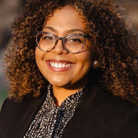 headshot of a woman in a printed shirt and black blazer with tortoise shell glasses